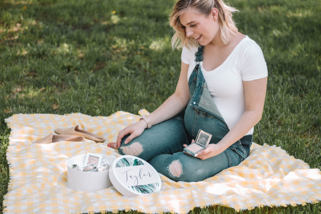 Taylor sitting on a picnic blanket with a box of makeup powders