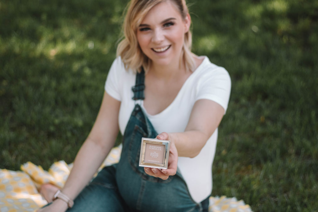 Taylor sitting on a picnic blanket with a box of makeup powders